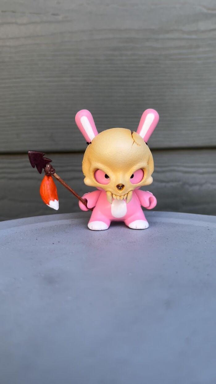 Quirky sculpture of a pink bunny with a skull head holding an arrow, showcasing an artist's unique personality-filled design.