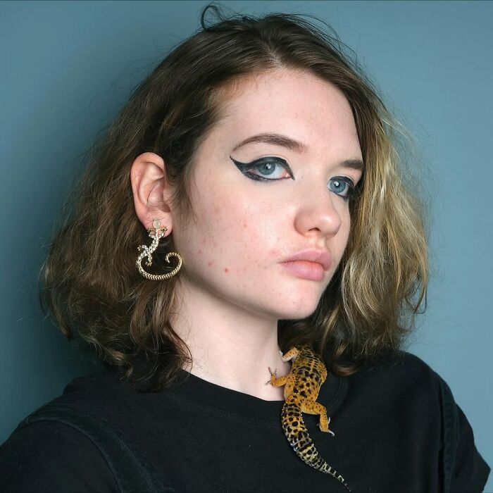 Young woman with bold eye makeup and a leopard gecko on her shoulder, showcasing pets and humans who look alike.