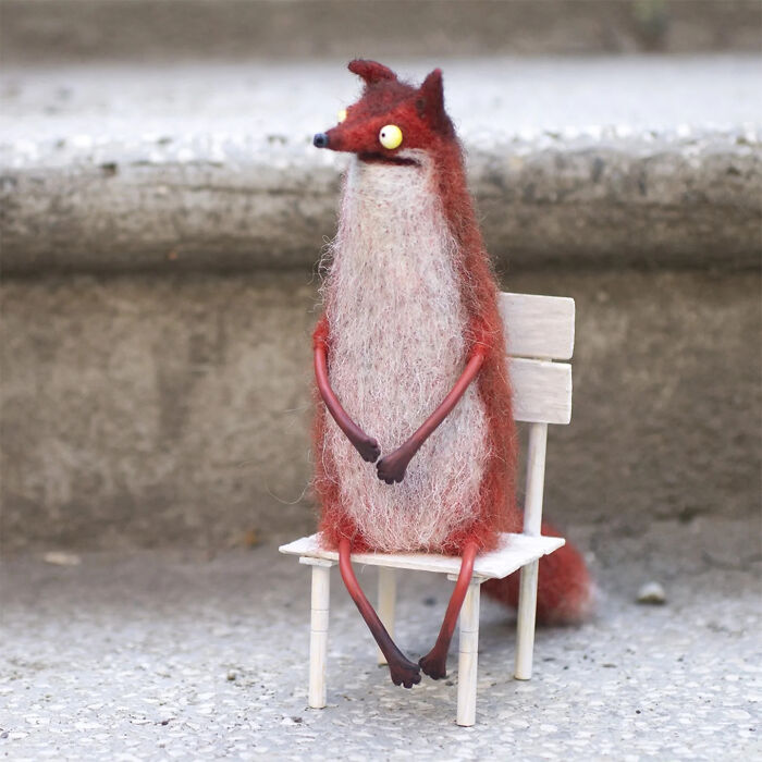 Handmade creature toy resembling a quirky red fox with large eyes sitting on a small white wooden chair outdoors.