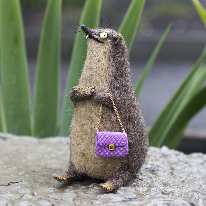 Handmade creature toy with quirky facial features holding a purple purse, showcasing adorably strange artistic design.