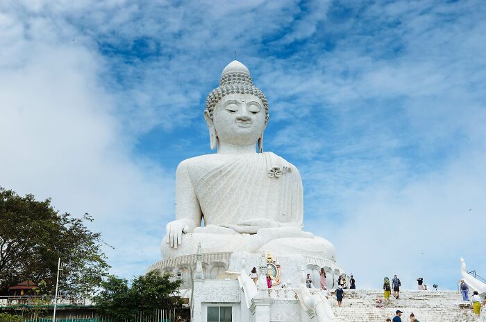 Large white Buddha sculpture against a blue sky with visitors around, showcasing spectacular sculptures across the globe.