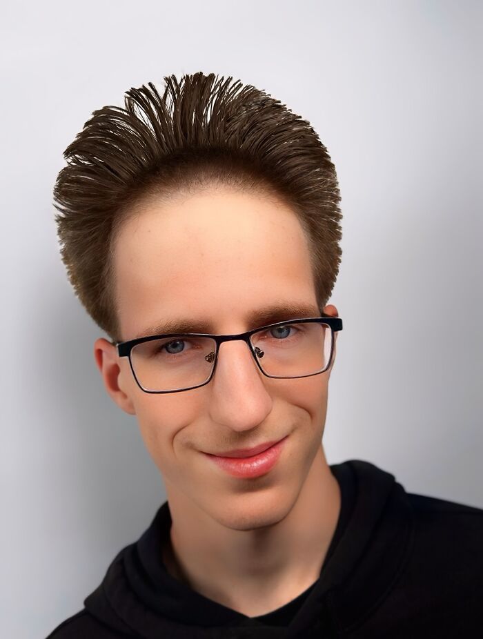 Young man with bold barber haircut styled upwards, wearing glasses and a black hoodie against a plain background Young man with bold barber haircut styled upwards, wearing glasses and a black hoodie against a plain background