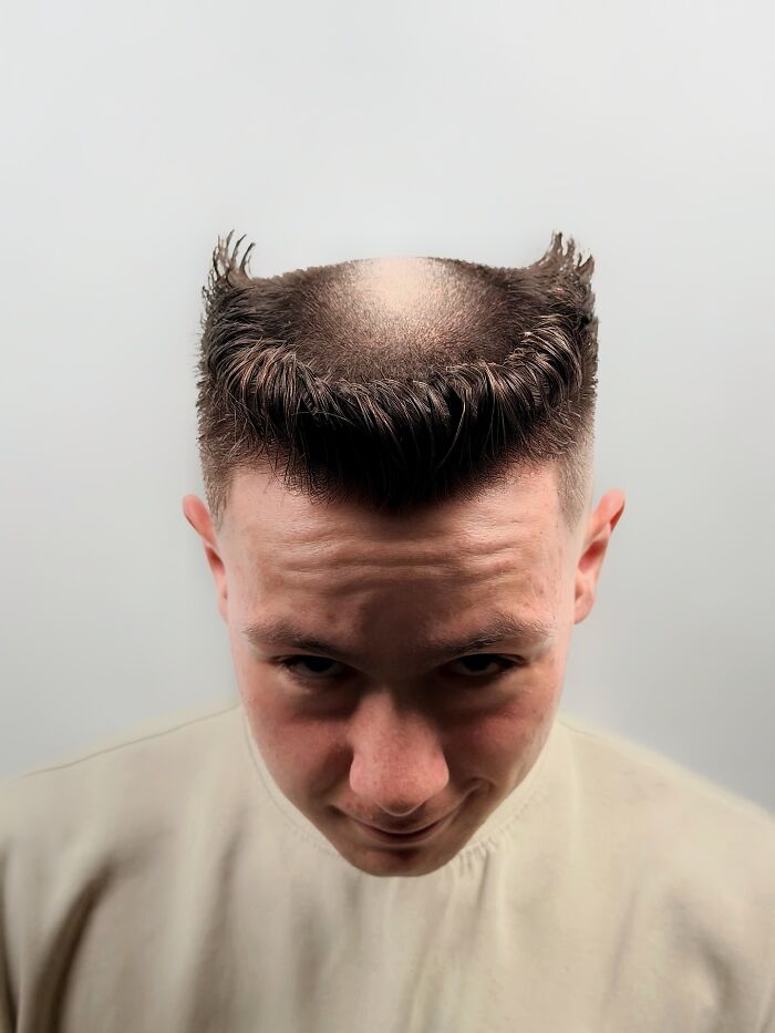 Man with a bold barber haircut featuring a unique styled top and shaved sides against a plain background