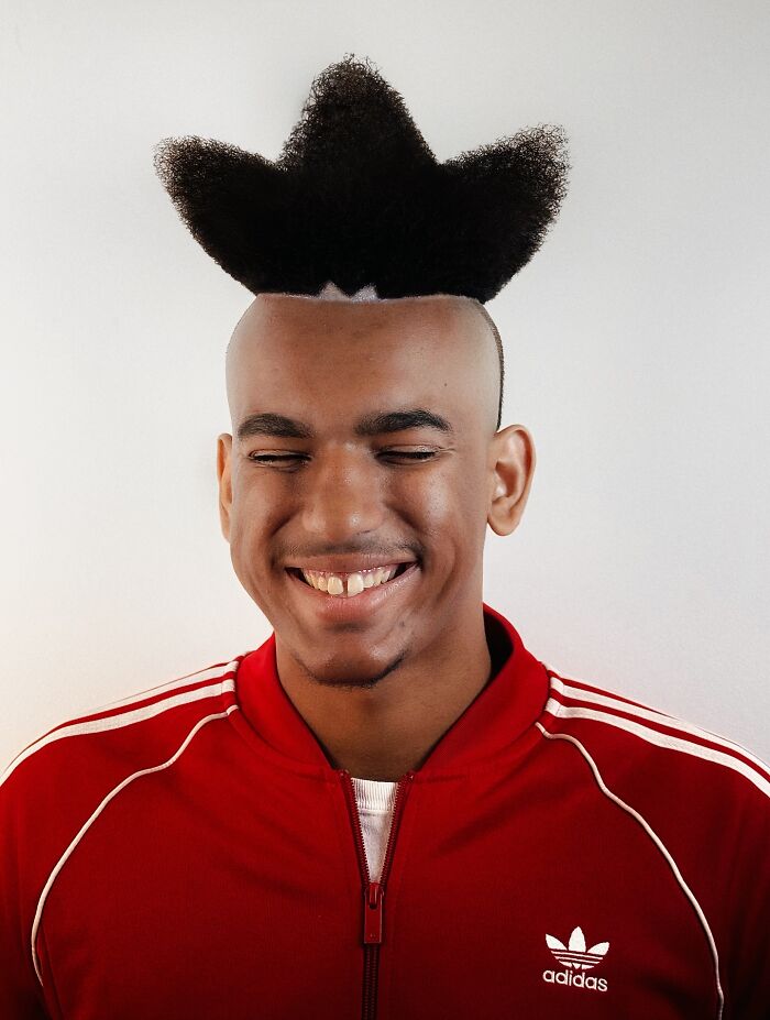 Young man with a bold barber haircut styled into a star shape, wearing a red Adidas jacket and smiling with eyes closed