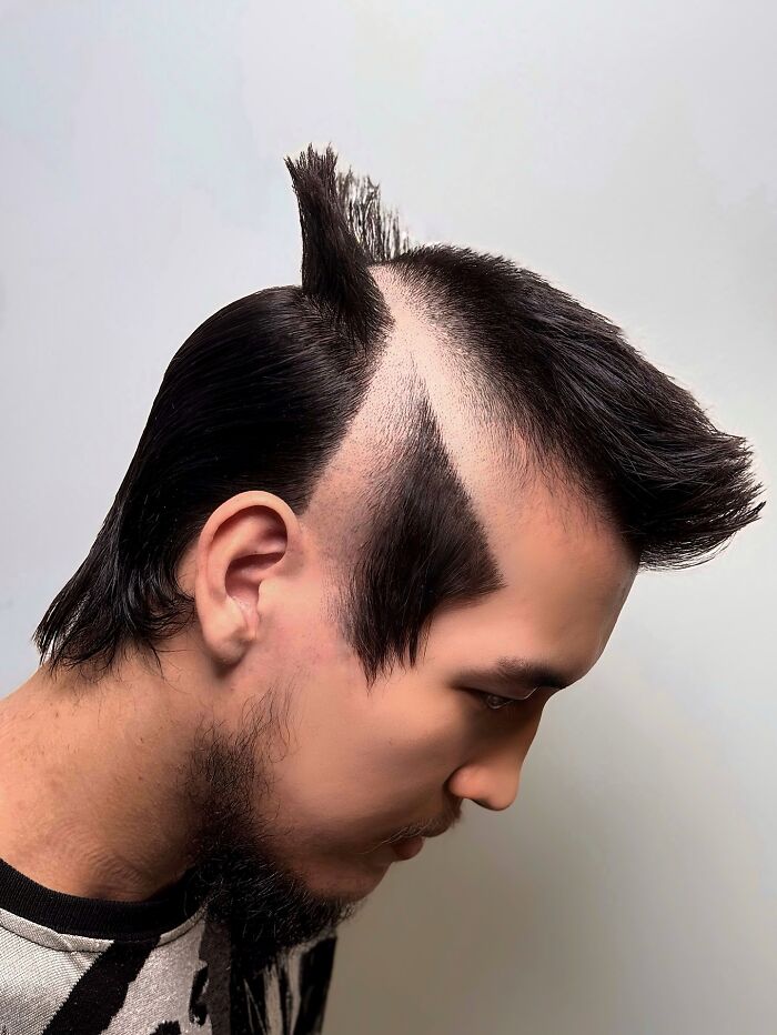 Man with bold barber haircut featuring sharp geometric shaved lines and styled spikes on dark hair against plain background