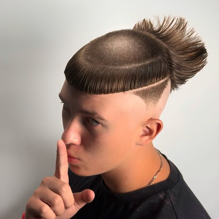 Young man with a bold barber haircut featuring a sharp line design and textured spiked hair on top against a plain background Young man with a bold barber haircut featuring a sharp line design and textured spiked hair on top against a plain background