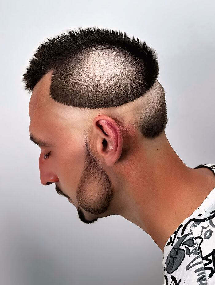 Man with a bold barber haircut featuring a unique shaved pattern with short spiked hair on top and artistic beard styling.