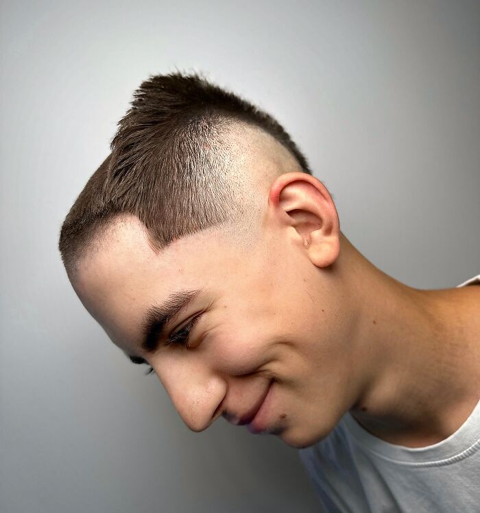 Young man with a bold barber haircut featuring sharp edges and a high fade smiling against a plain background