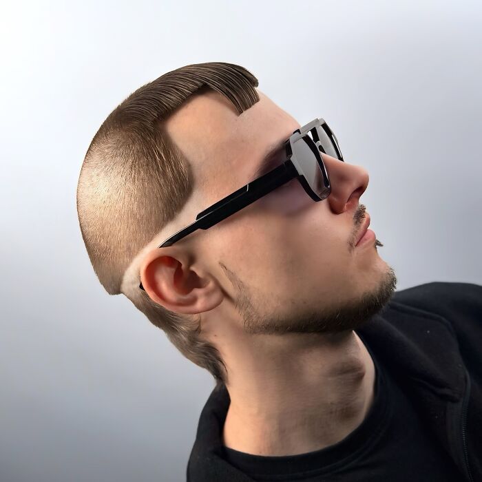 Profile of a young man wearing sunglasses showcasing a bold barber haircut with sharp edges and unique styling.
