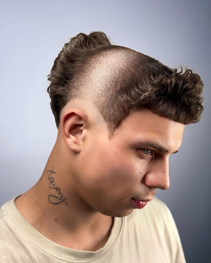 Young man with a bold barber haircut featuring shaved sides and curly top, showcasing next level hair design and style.