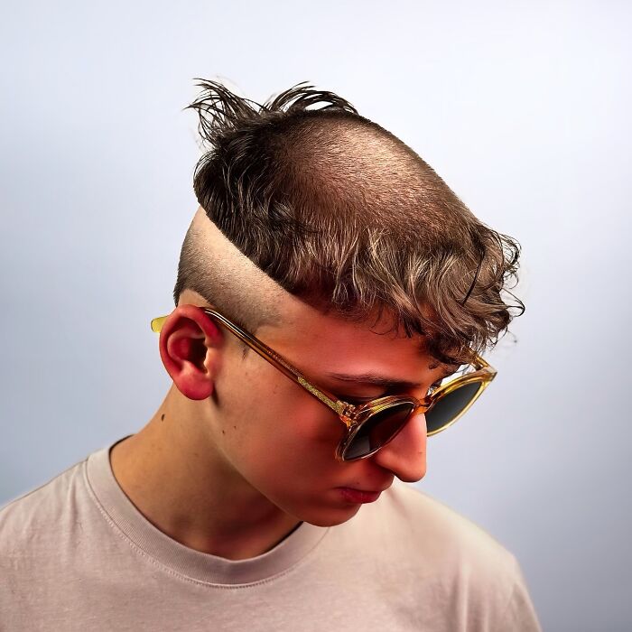 Young man with a bold barber haircut featuring shaved sides and a unique textured top wearing sunglasses.