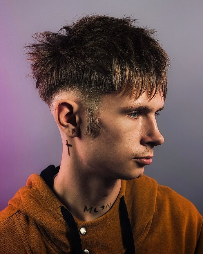 Young man with a bold barber haircut featuring a textured top and faded sides, wearing an orange hoodie against a neutral background.