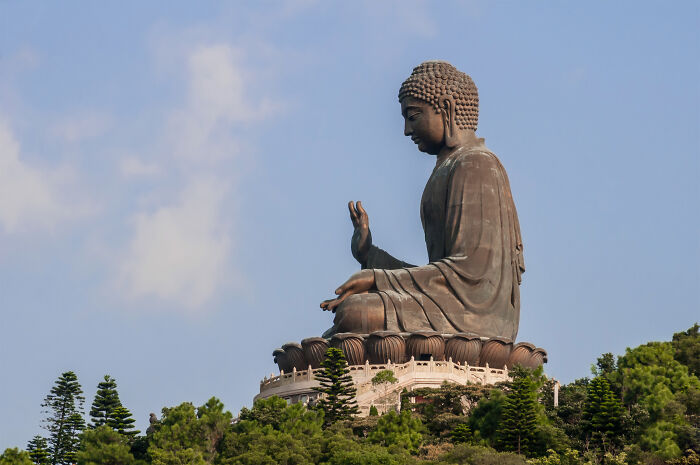 Large Buddha sculpture seated outdoors on a hill surrounded by trees, a spectacular sculpture attracting global travelers.