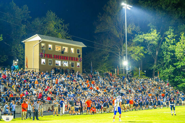 Crowded football stadium with players and spectators under bright lights, relating to missing football coach case mystery. Crowded football stadium with players and spectators under bright lights, relating to missing football coach case mystery.