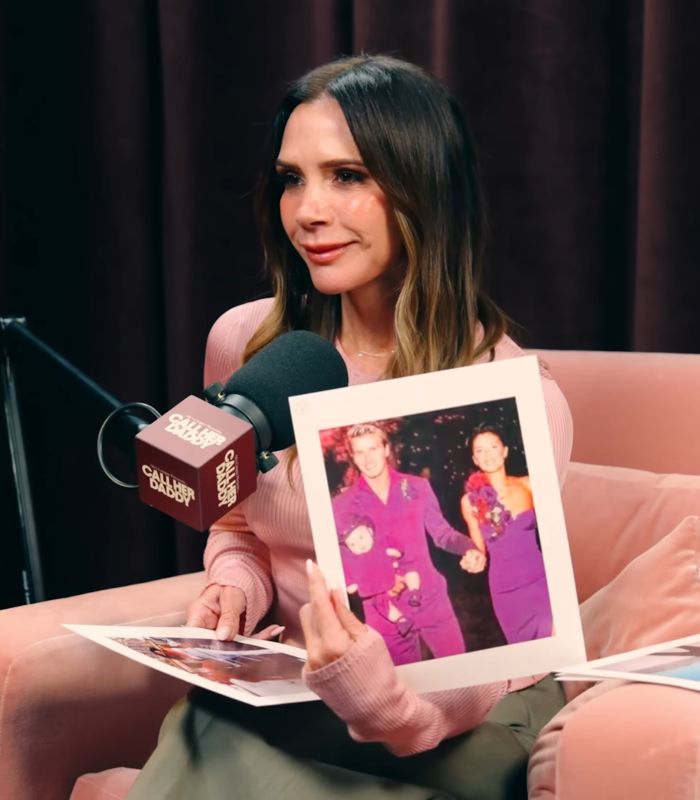 Victoria Beckham speaking into a podcast microphone, holding a family photo after David receives Sir title. Victoria Beckham speaking into a podcast microphone, holding a family photo after David receives Sir title.