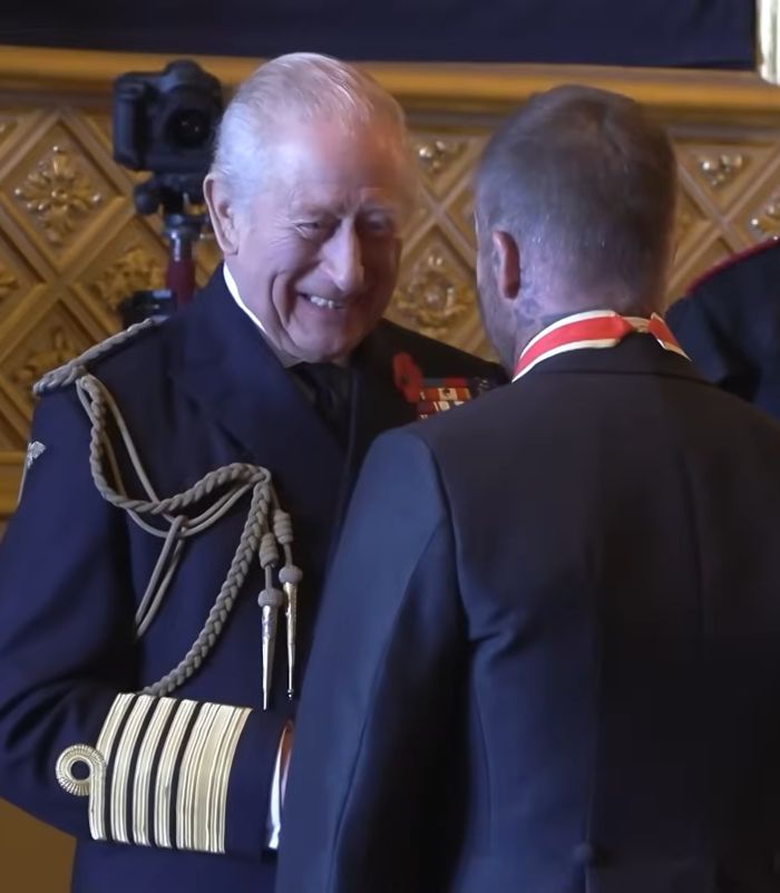 Man receiving a formal honor in uniform with Victoria Beckham unveiling new name after David's Sir title recognition. Man receiving a formal honor in uniform with Victoria Beckham unveiling new name after David's Sir title recognition.