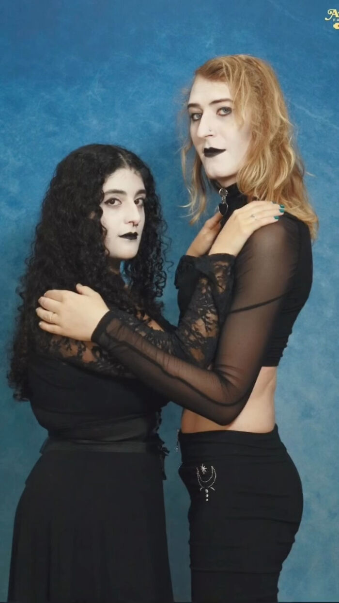 Two people dressed in black with Gothic makeup posing in an awkward studio pic against a blue backdrop.