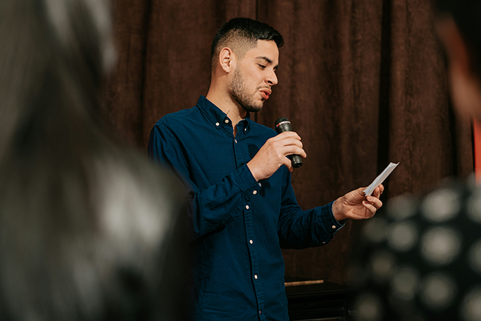 Man holding a microphone and note speaking in front of a small audience, expressing caretaker frustration and guilt trips. Man holding a microphone and note speaking in front of a small audience, expressing caretaker frustration and guilt trips.