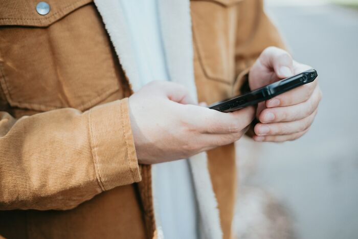 Person in a brown jacket holding a smartphone, symbolizing ways people found out their significant other is unfaithful.