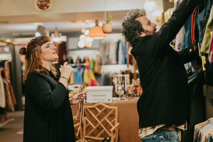 Two workers sharing unprofessional things while organizing clothes in a casual retail store setting.