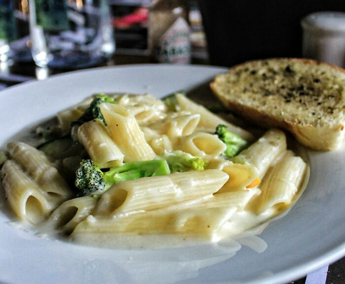 Creamy penne pasta with broccoli served on a white plate alongside a slice of seasoned garlic bread, highlighting home cooks’ knife skills.