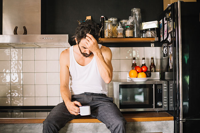 Grieving dad sitting in kitchen, holding a cup, looking distressed while trying to make daughter’s birthday special.
