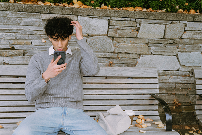 Young man on a bench looking frustrated while using phone, symbolizing caretaker snapping after guilt trips and sacrifice. Young man on a bench looking frustrated while using phone, symbolizing caretaker snapping after guilt trips and sacrifice.
