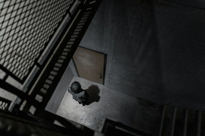 Person standing alone in a dimly lit concrete stairwell, creating an eerie scene captured by surveillance cameras.