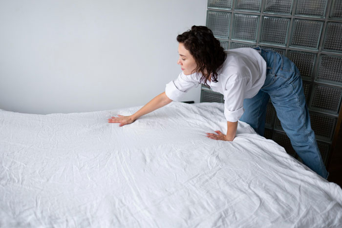 Pregnant woman preparing a bed with white sheets in a modern room, relating to air mattress and sleeping arrangements.