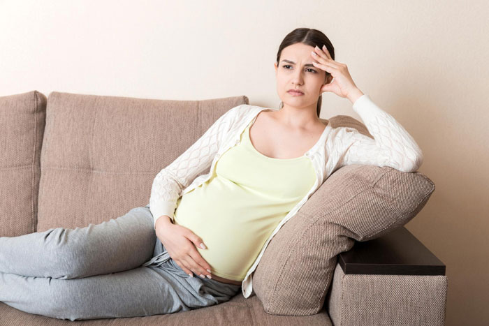 Pregnant woman looking upset while reclining on a couch, reflecting feelings of offense and discomfort.