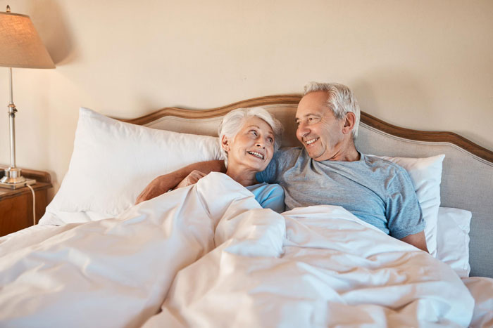 Elderly couple smiling together in bed, representing a scene related to pregnant SIL offended over sleeping arrangements.