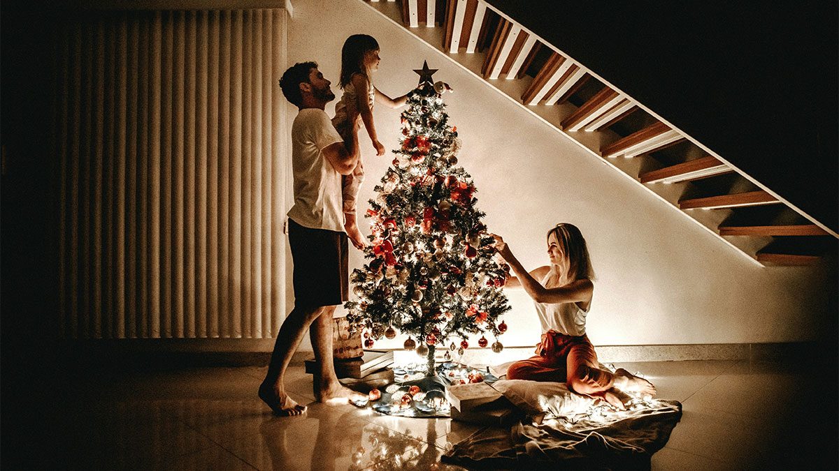 Family decorating a lit Christmas tree indoors, highlighting a festive moment amidst concerns over watermark removal on photos.