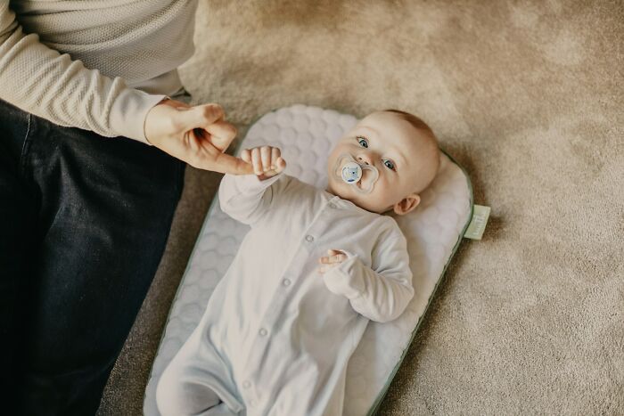 Baby lying on a cushion holding an adult’s finger, representing subtle signs that scream they’re cheating once noticed.