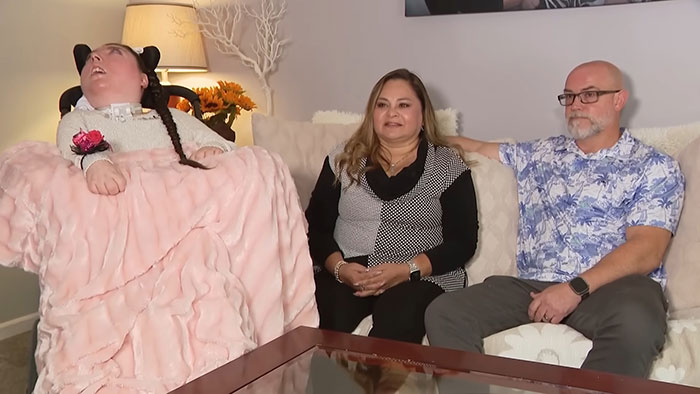 Woman born without most of her brain sits with family on couch, sparking discussion about her life and condition. Woman born without most of her brain sits with family on couch, sparking discussion about her life and condition.