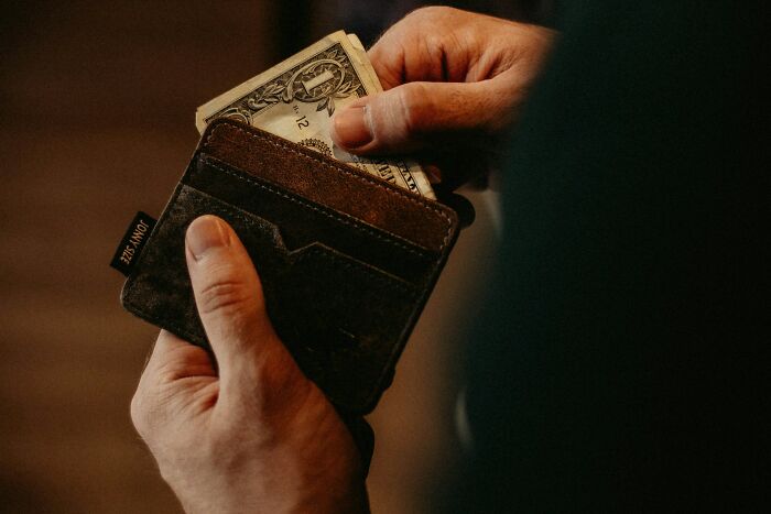 Person holding a brown leather wallet with a dollar bill, illustrating funny and serious moments parents face raising monsters.