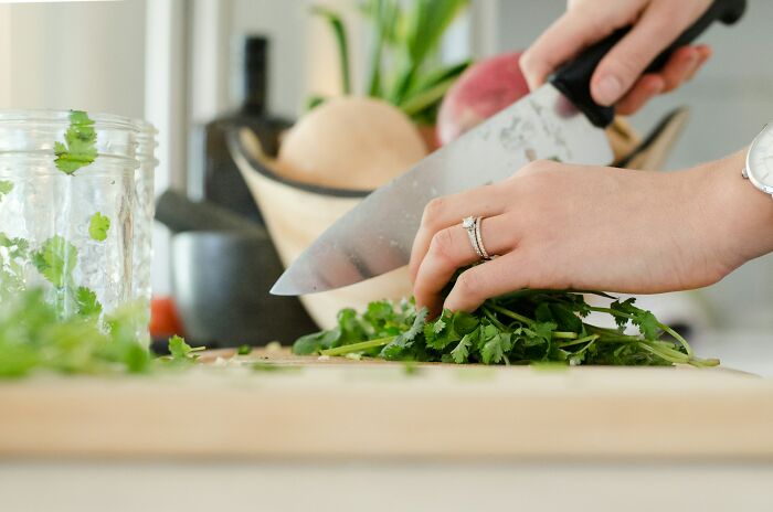 Hands sharpening knives while chopping fresh herbs on a cutting board in a bright kitchen setting.