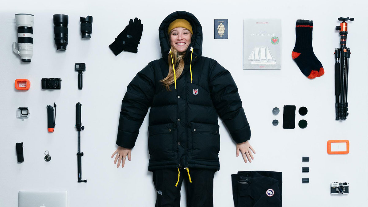 Person surrounded by neatly arranged camera gear, travel items, and clothing illustrating all things knolled for visual order.
