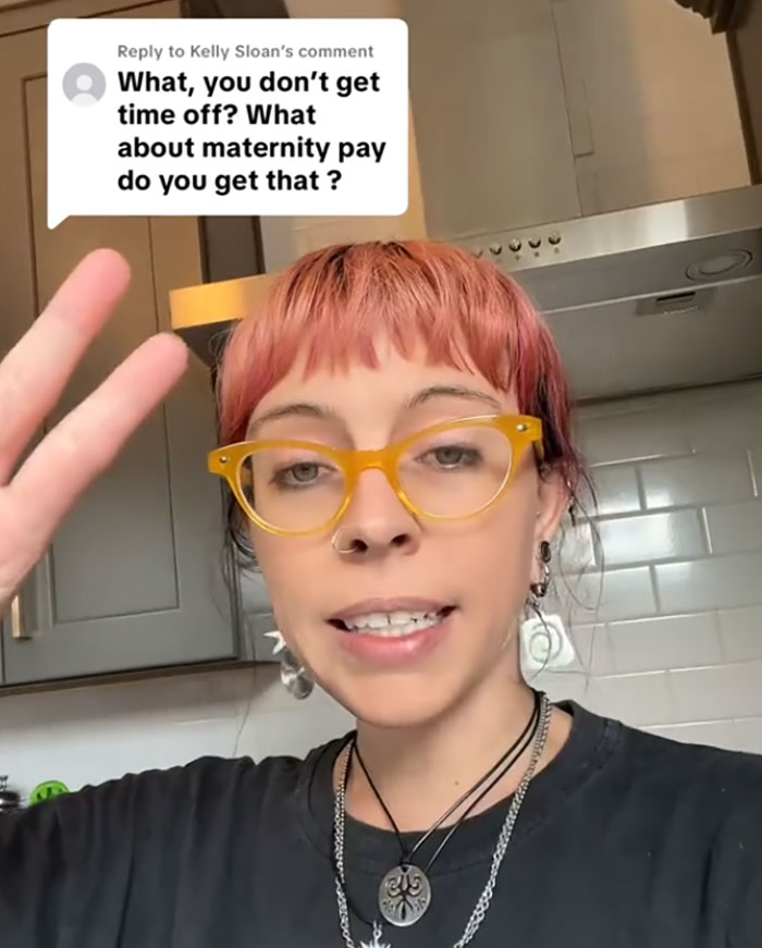 Young woman with pink hair and yellow glasses discusses pay for ambulance rides in a kitchen setting.