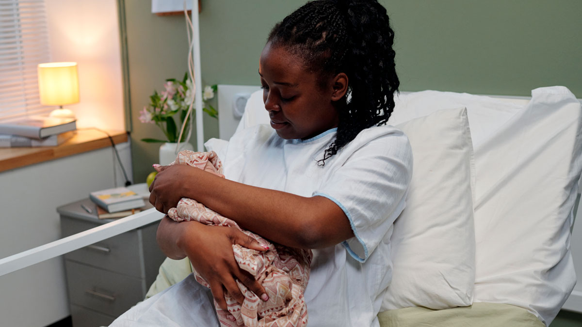 Woman in hospital gown holding newborn baby in a hospital room highlighting pay for ambulance rides issue