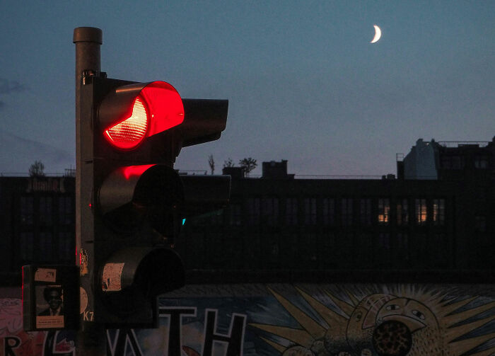 Red traffic light glowing at dusk with crescent moon in the sky, symbolizing Americans sharing great things about the US.