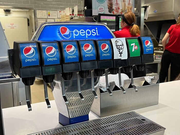Soda fountain machine with Pepsi, 7 Up, and KFC branding inside a US fast food restaurant setting.