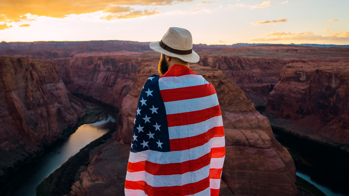 Man wrapped in an American flag overlooking scenic canyon landscape at sunset, showcasing the great things about the US.