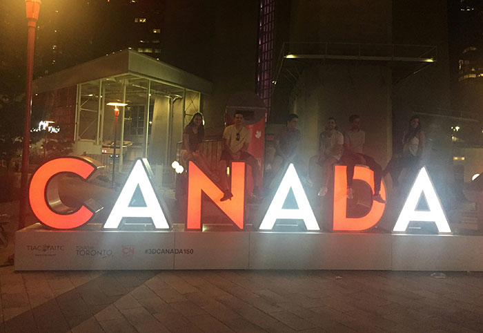 People sitting on illuminated Canada sign at night, illustrating American expats noticing differences in Canada.