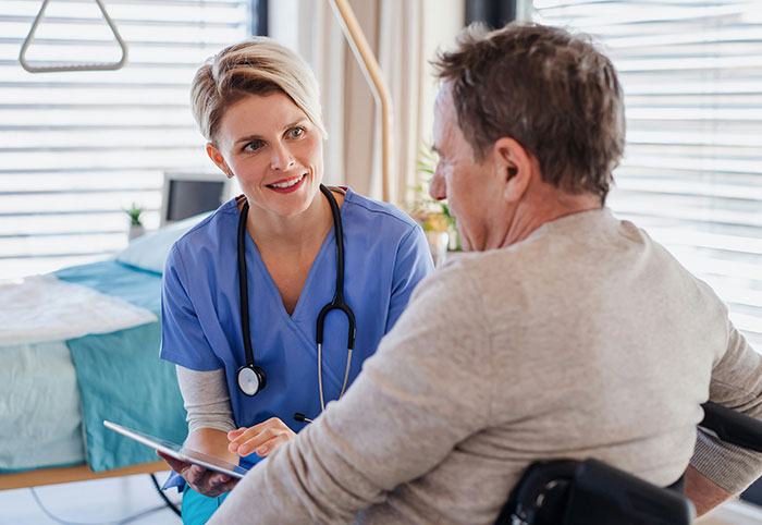Nurse in blue scrubs talking with male patient in a wheelchair, representing American expats' experiences in Canada.