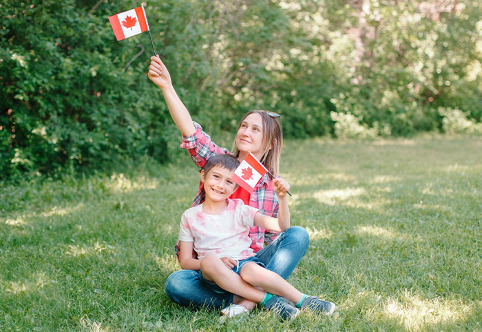 Mother and child sitting on grass in a park, holding Canadian flags, enjoying outdoors as American expats in Canada.