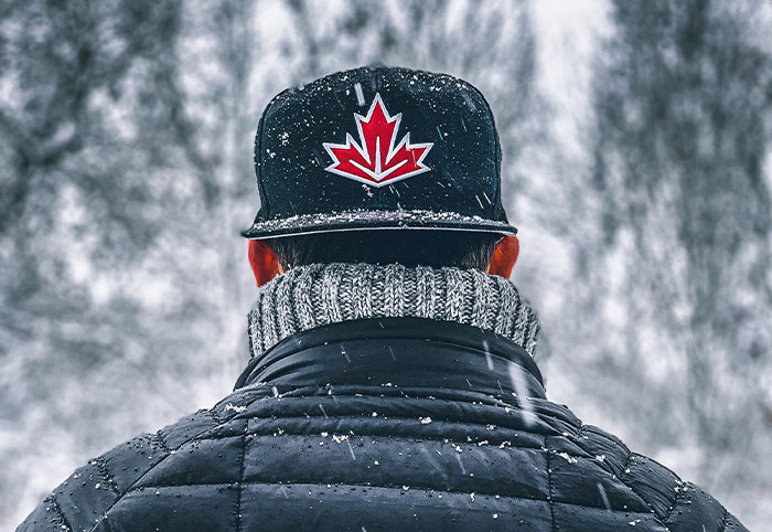 Person wearing a black cap with a red maple leaf in snowy Canadian landscape, highlighting American expats in Canada.