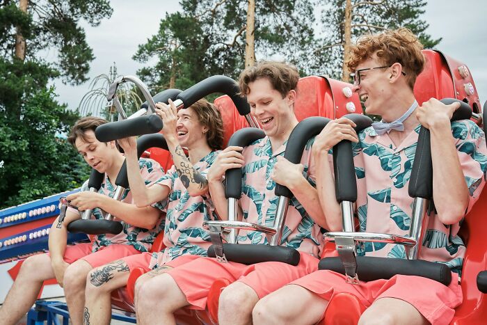 Four friends wearing matching tropical shirts laugh together on a red amusement park ride, capturing funny moments with loved ones.