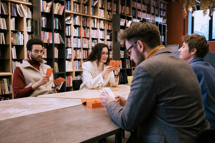 Group of friends playing cards in a cozy library setting, capturing moments of funny and accidental hurt during game time.