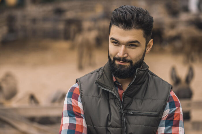 Bearded man in a plaid shirt and vest outdoors, illustrating bizarre patient behavior under the effects of anesthesia.