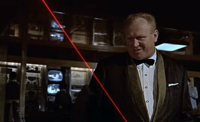 Man in tuxedo in a dark room with a red laser beam, illustrating patients under the effects of anesthesia.